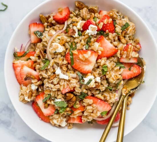 A strawberry farro salad in a serving bowl on top of a marble counter