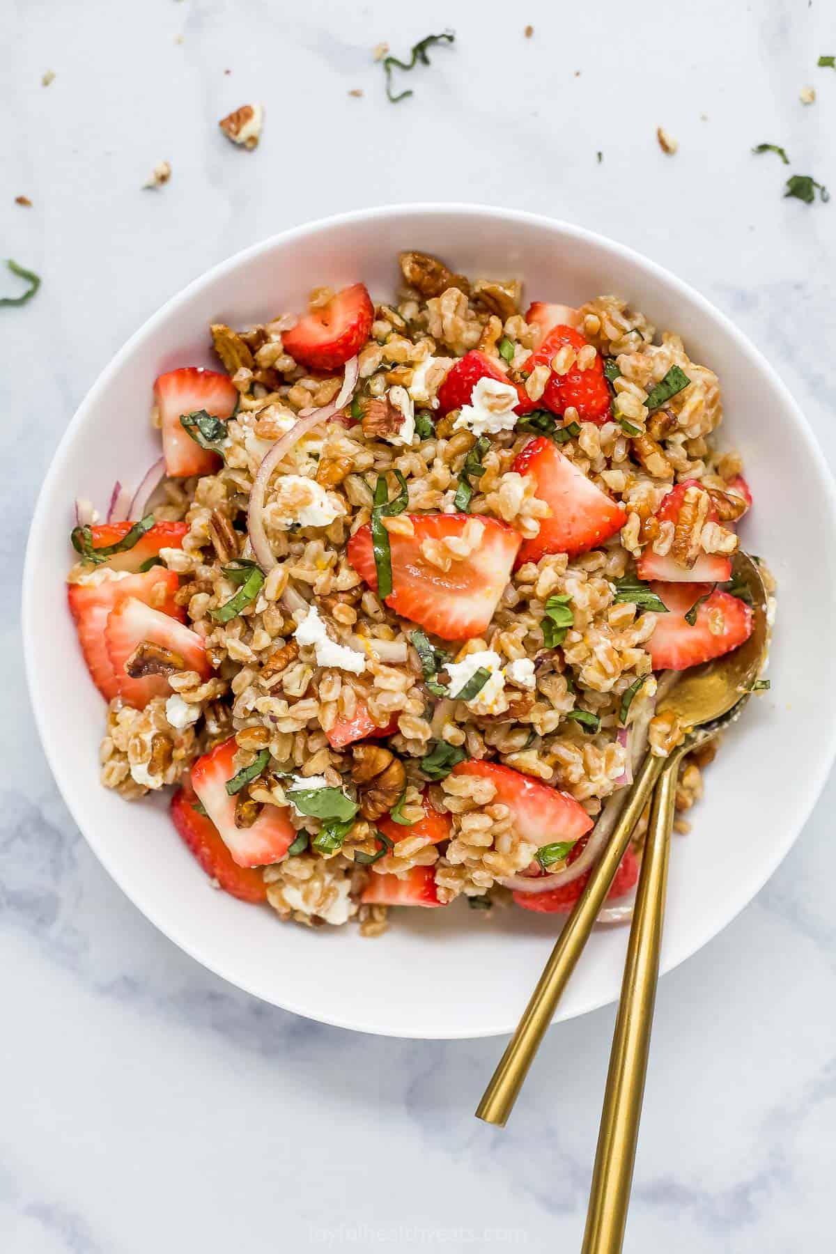 A strawberry farro salad in a serving bowl on top of a marble counter