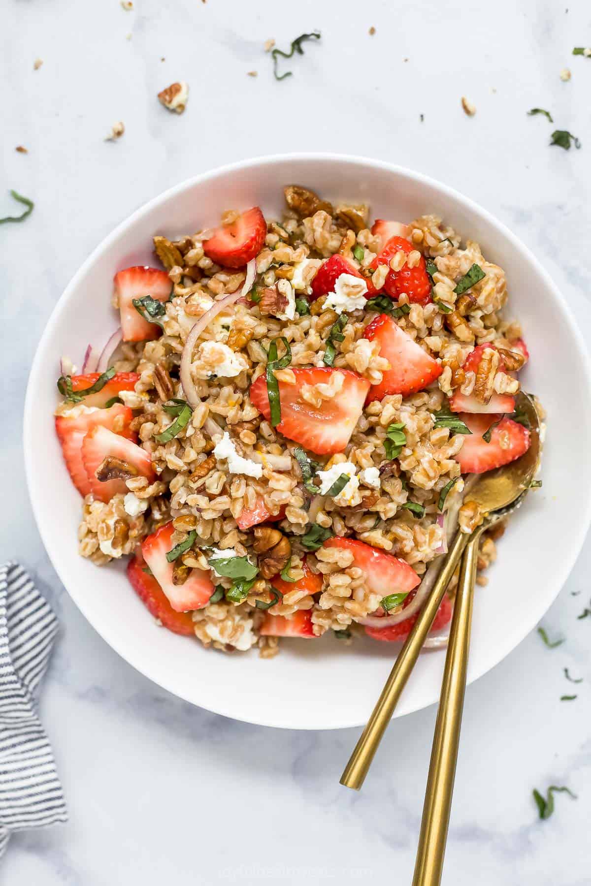 A bowl of strawberry farro salad on a kitchen countertop beside a cloth napkin