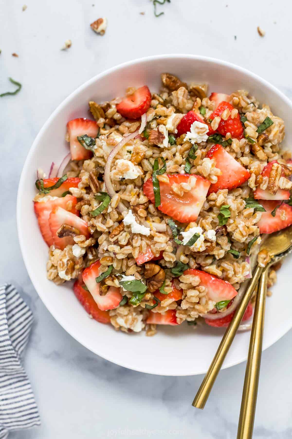 A close-up shot of a bowl of strawberry farro salad on a kitchen countertop