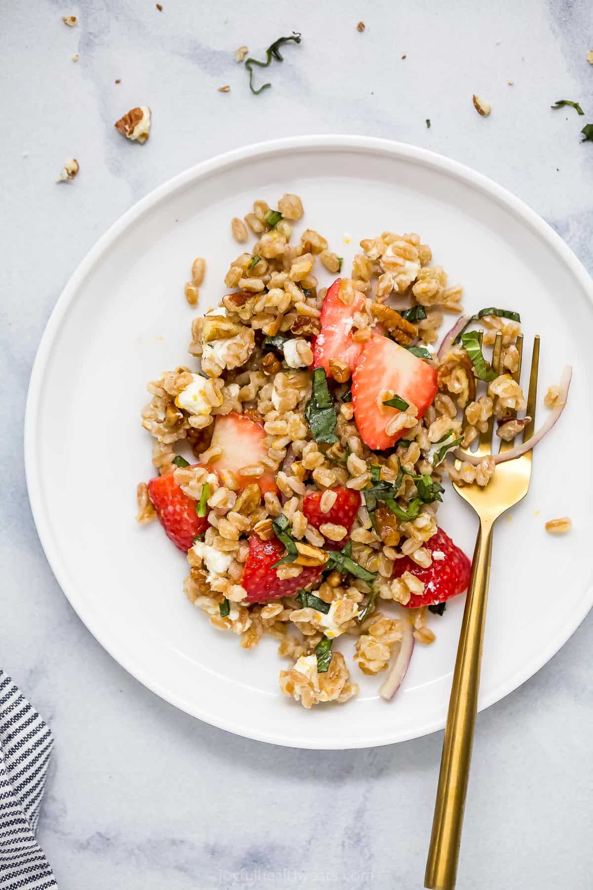 A serving of strawberry farro salad on a plate with a golden fork