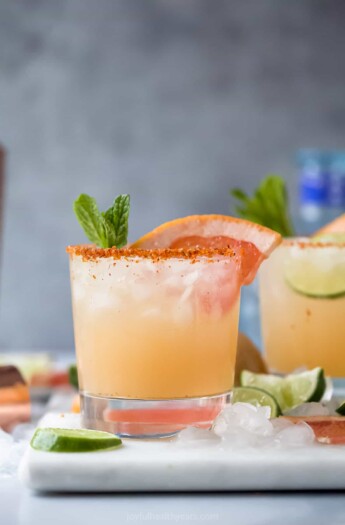 A homemade Paloma cocktail on top of a cutting board with a bottle of tequila blanco in the background