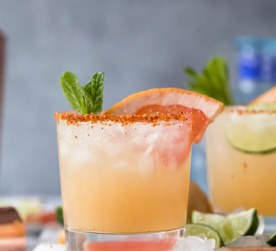 A homemade Paloma cocktail on top of a cutting board with a bottle of tequila blanco in the background