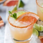 A grapefruit tequila mixed drink in a glass with ice and a tajín-coated rim