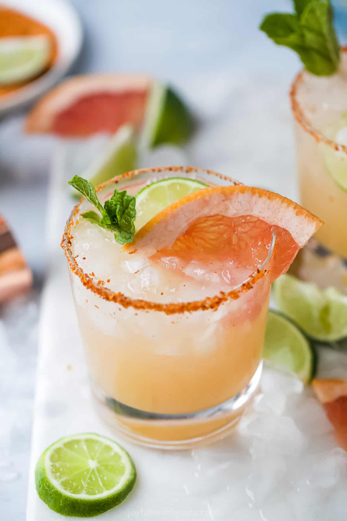 A grapefruit tequila mixed drink in a glass with ice and a tajín-coated rim