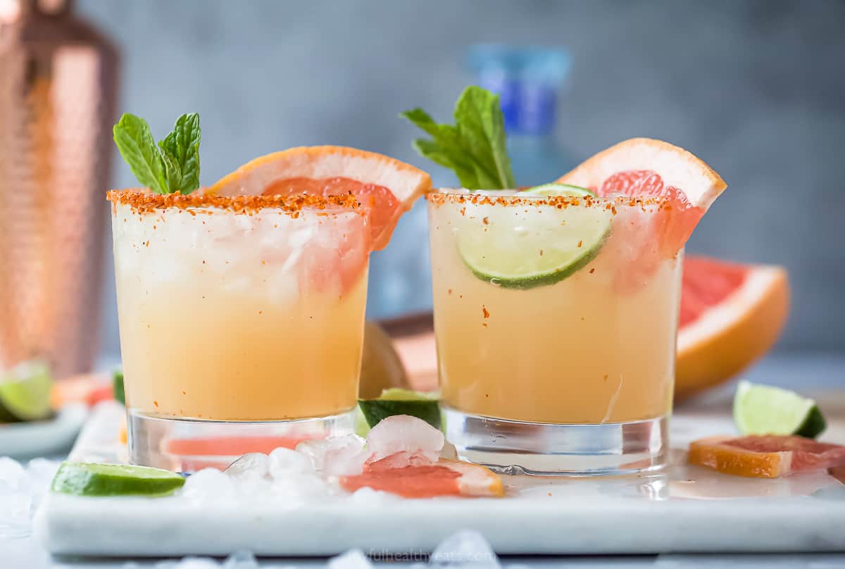 Two Paloma cocktails on a plastic cutting board with a cocktail shaker behind them