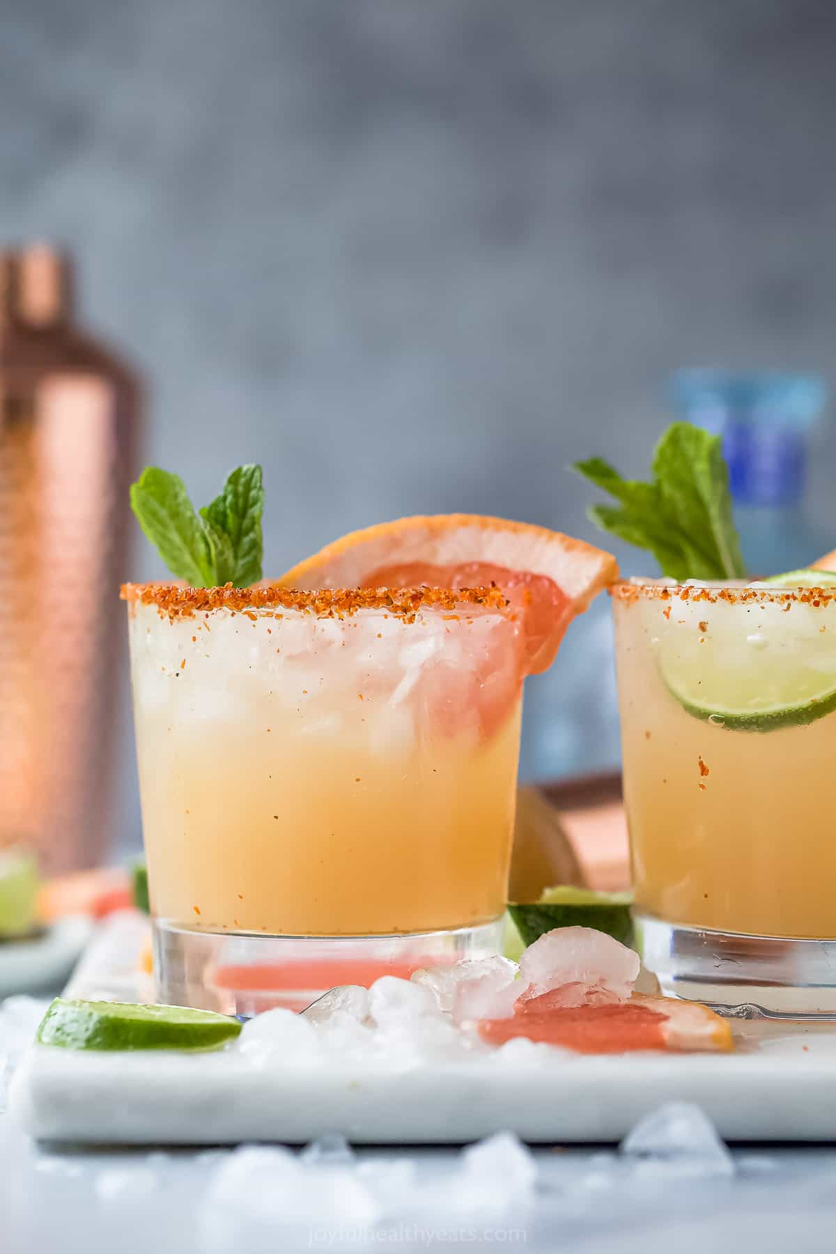 A Paloma cocktail on a cutting board beside a second cocktail and a couple of fresh citrus wedges