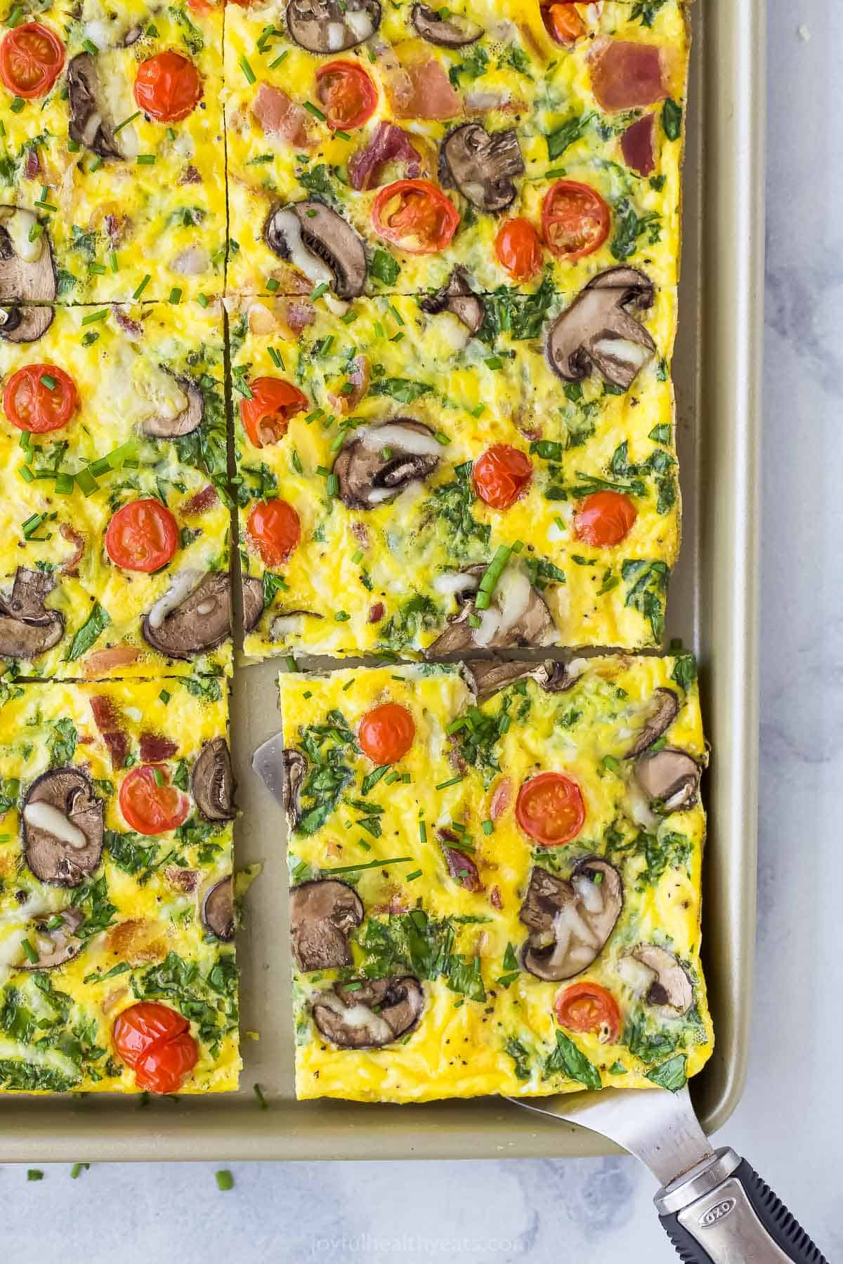 A piece of frittata being lifted off of a large baking sheet