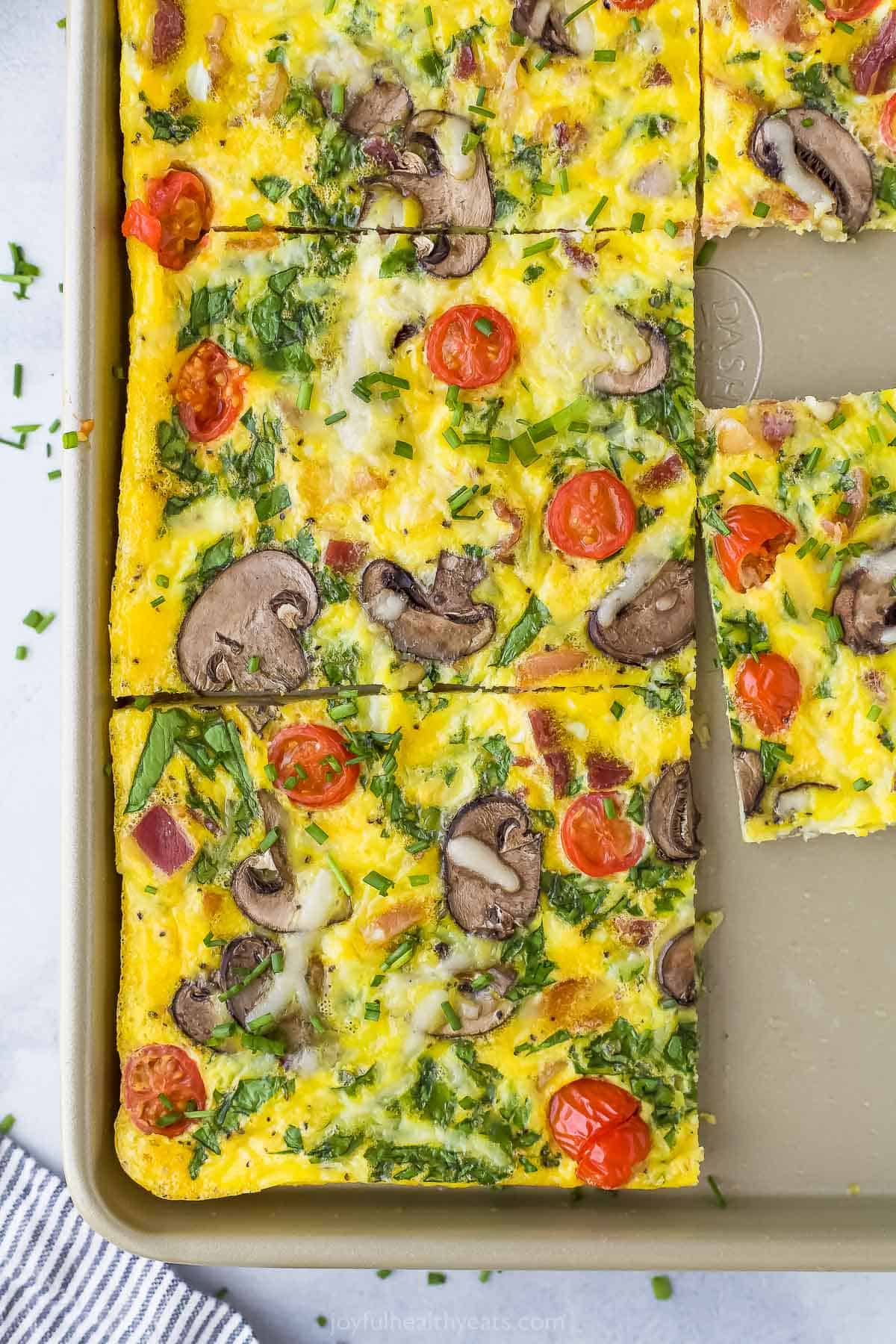 A spinach and egg frittata in a tan baking sheet with one piece removed