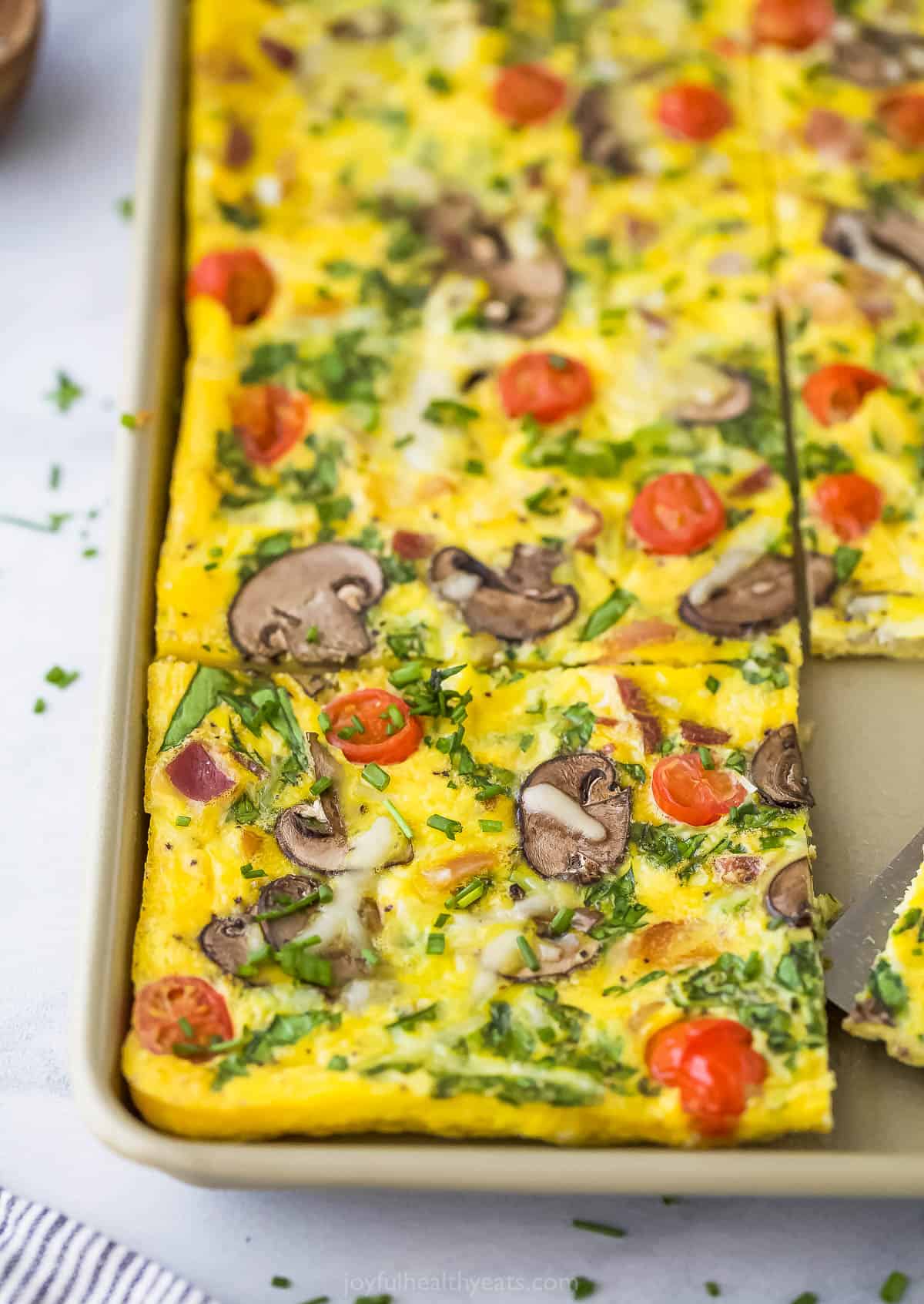 A baked egg frittata topped with bacon, spinach, mushrooms, cheese and tomatoes