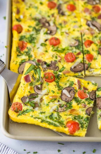 A metal serving spatula lifting up a slice of spinach frittata from a sheet pan