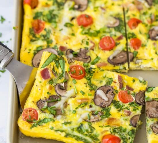 A metal serving spatula lifting up a slice of spinach frittata from a sheet pan