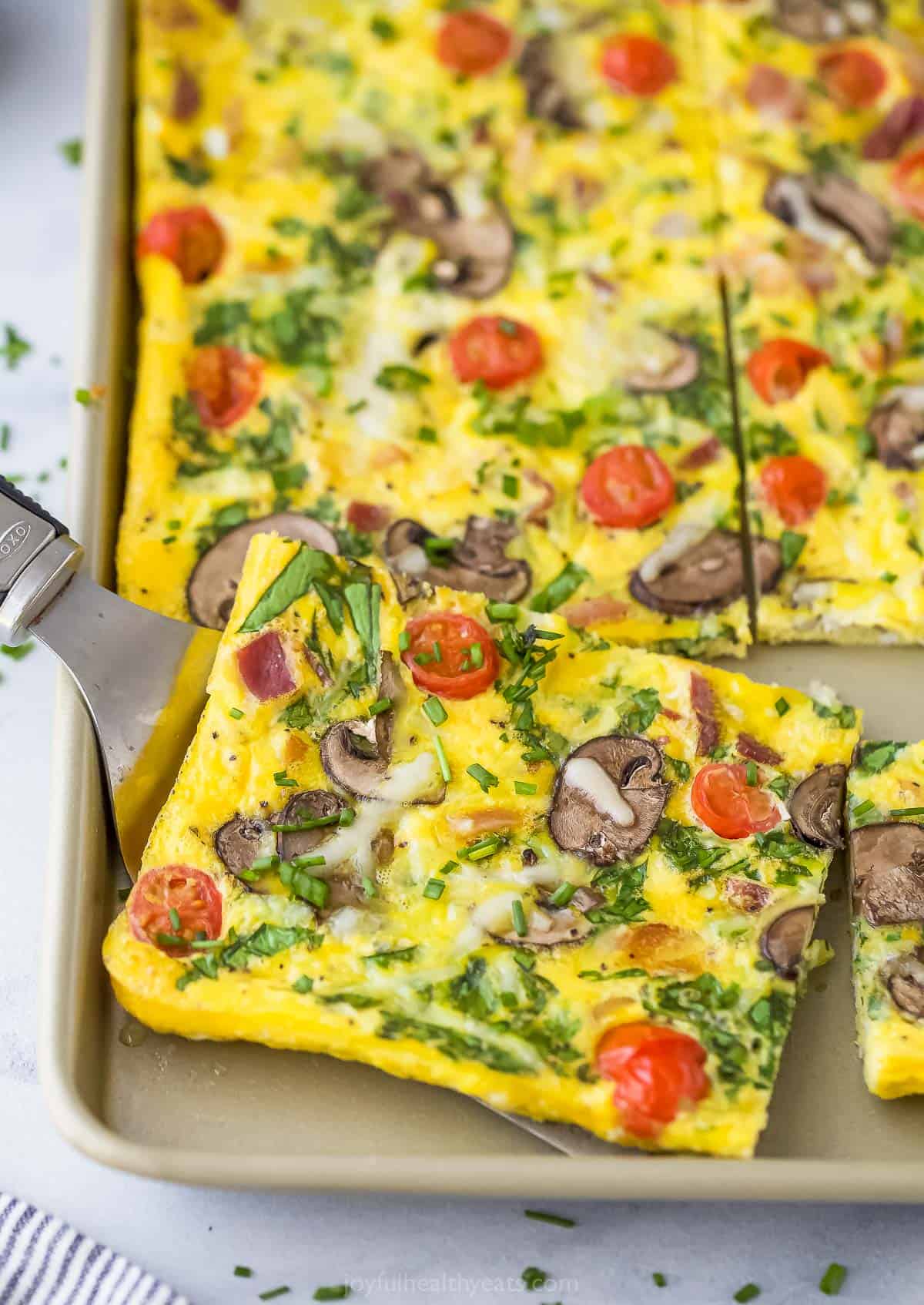 A metal serving spatula lifting up a slice of spinach frittata from a sheet pan