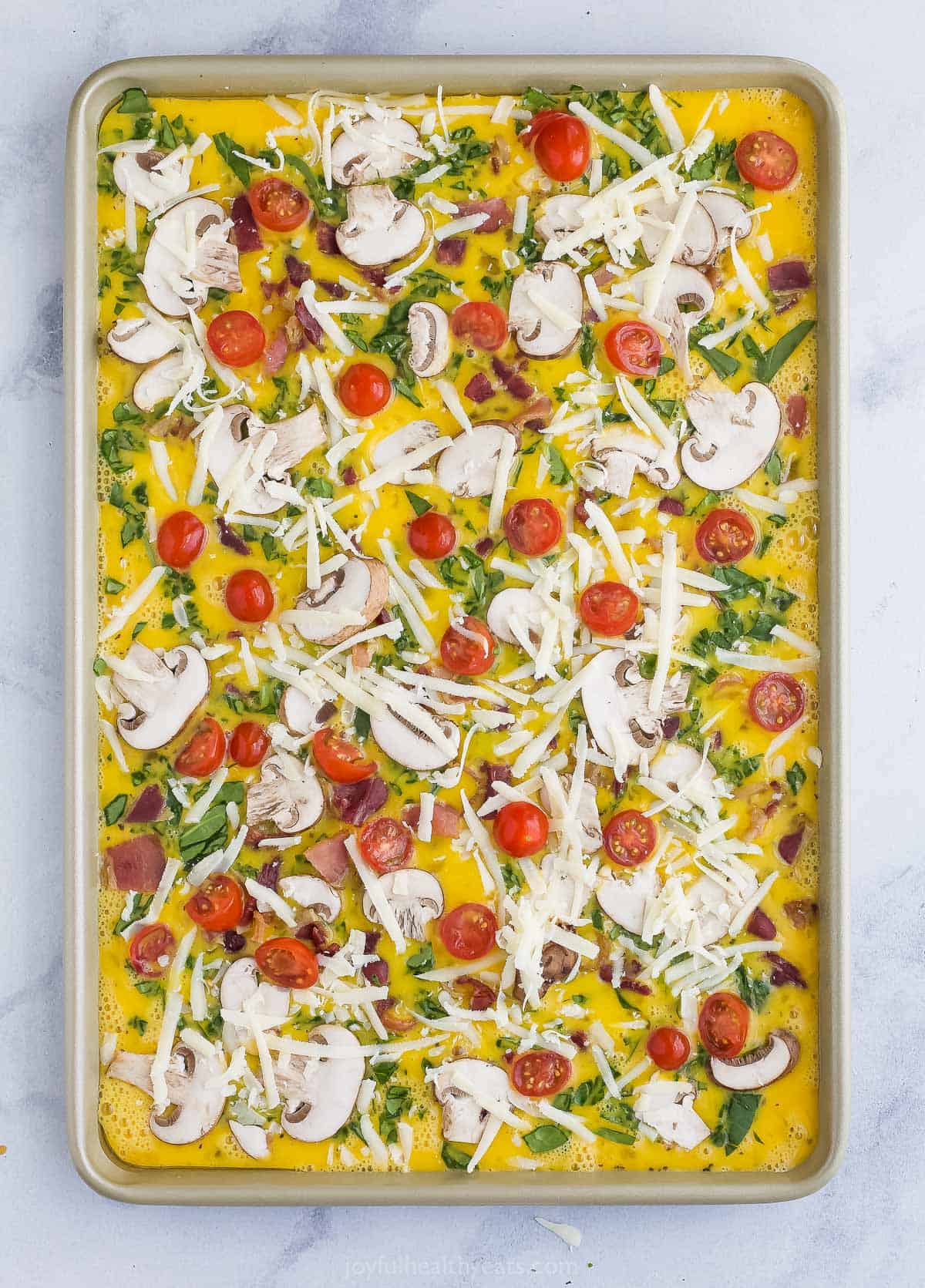Spinach frittata batter in a baking sheet after all of the toppings have been added