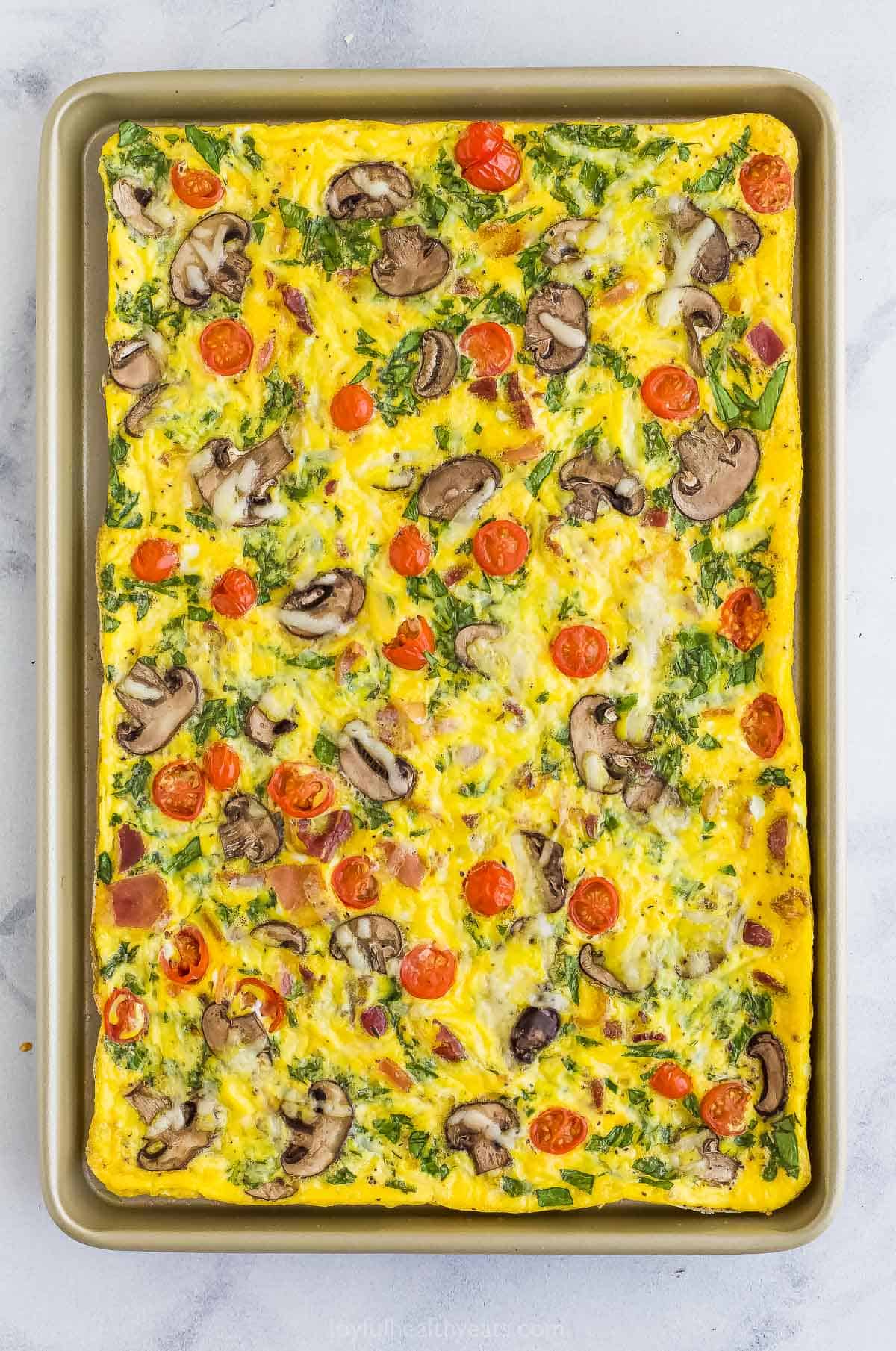 A baked spinach frittata in a baking sheet on top of a marble counter