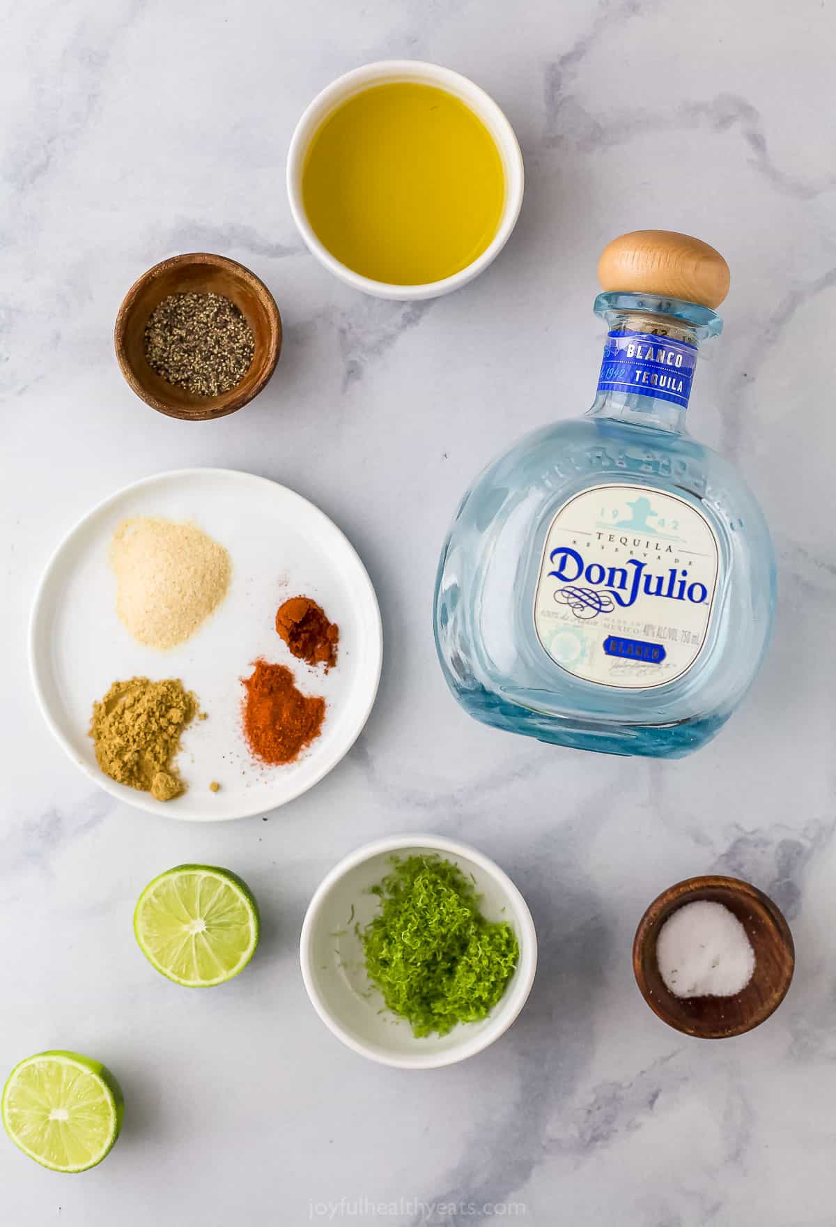 A bottle of tequila, a halved lime, garlic powder and the rest of the grilled chicken ingredients on a kitchen countertop