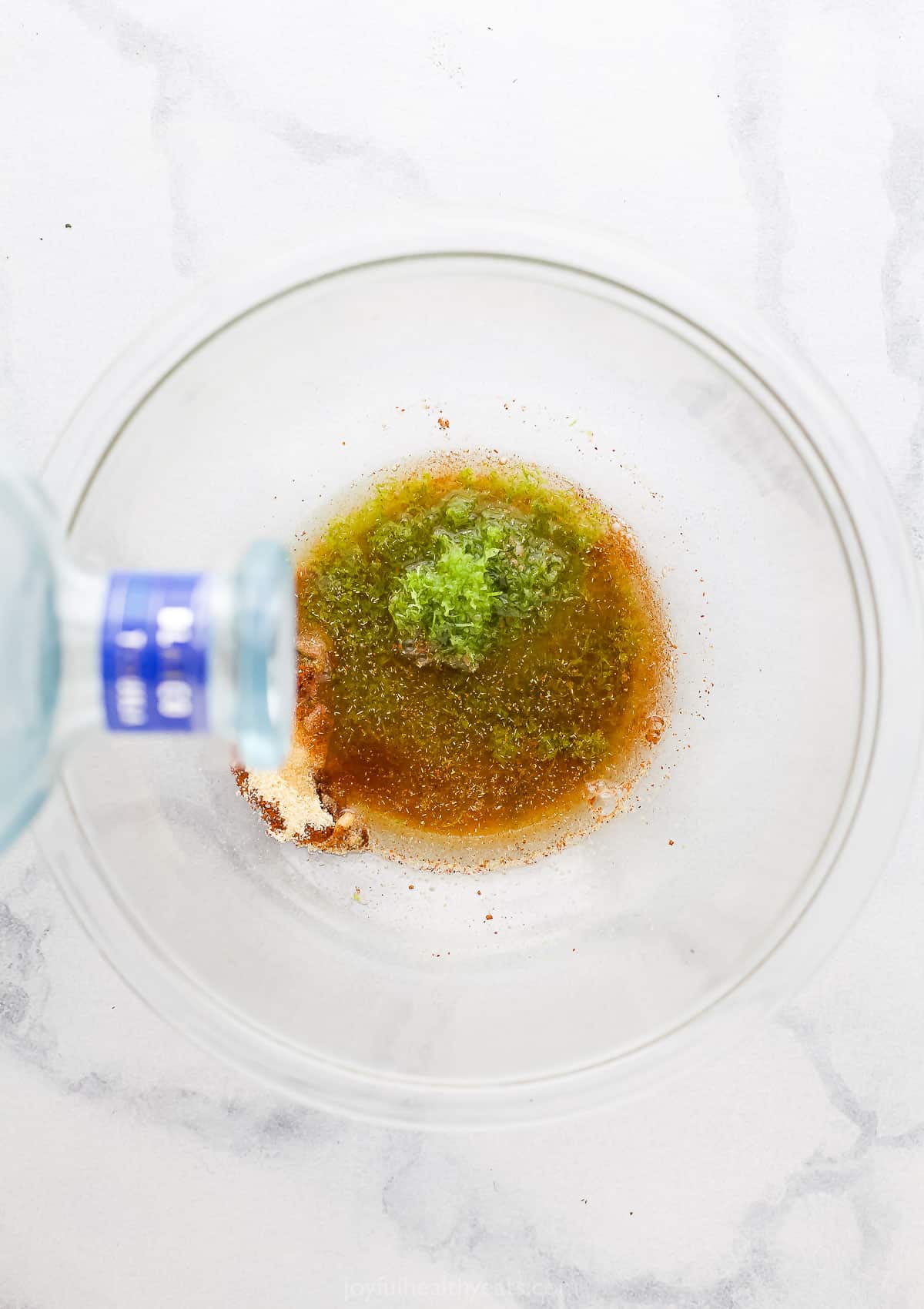 Tequila being poured into a large glass bowl full of seasonings