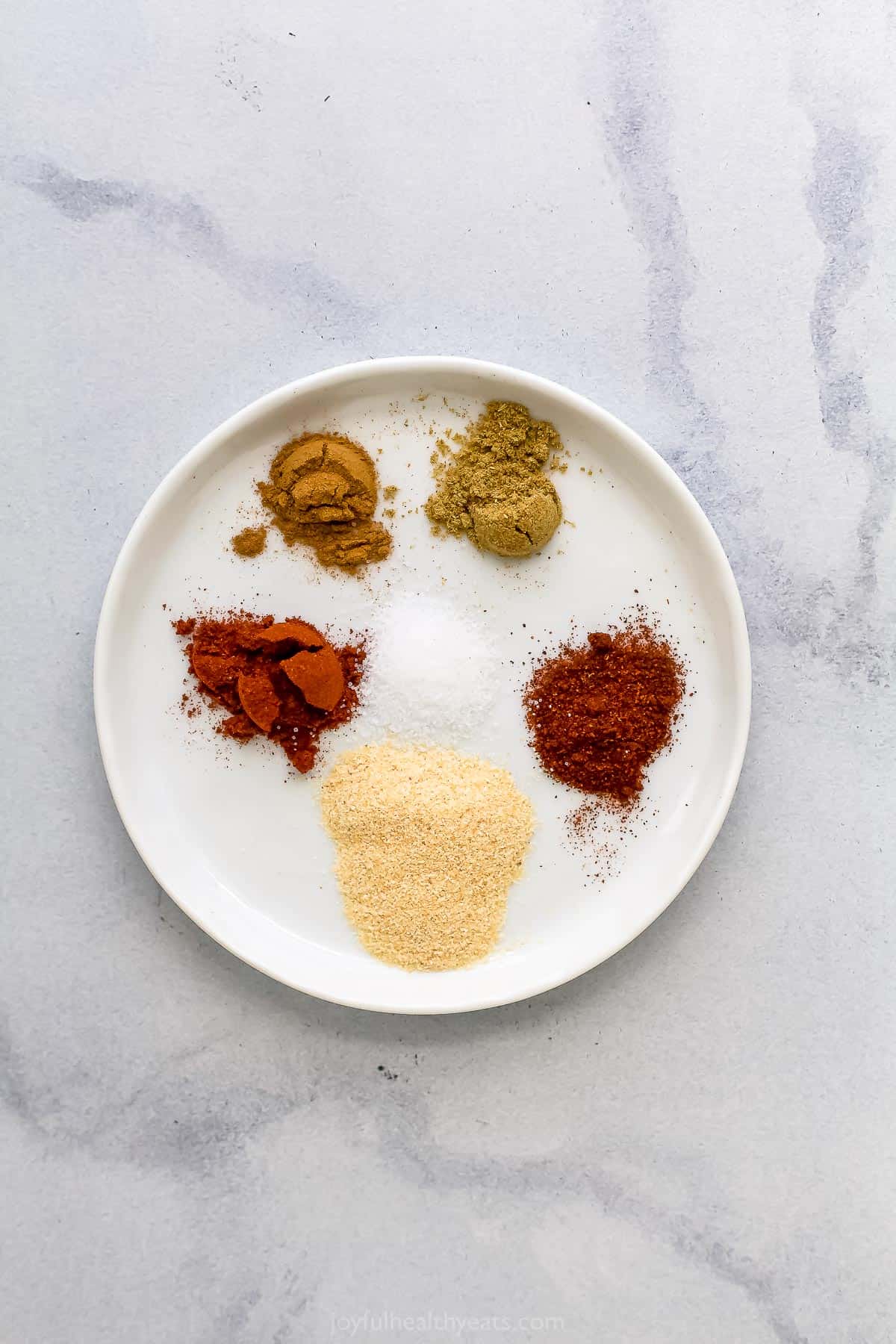 All of the spice rub ingredients in a small dish on a marble kitchen countertop.