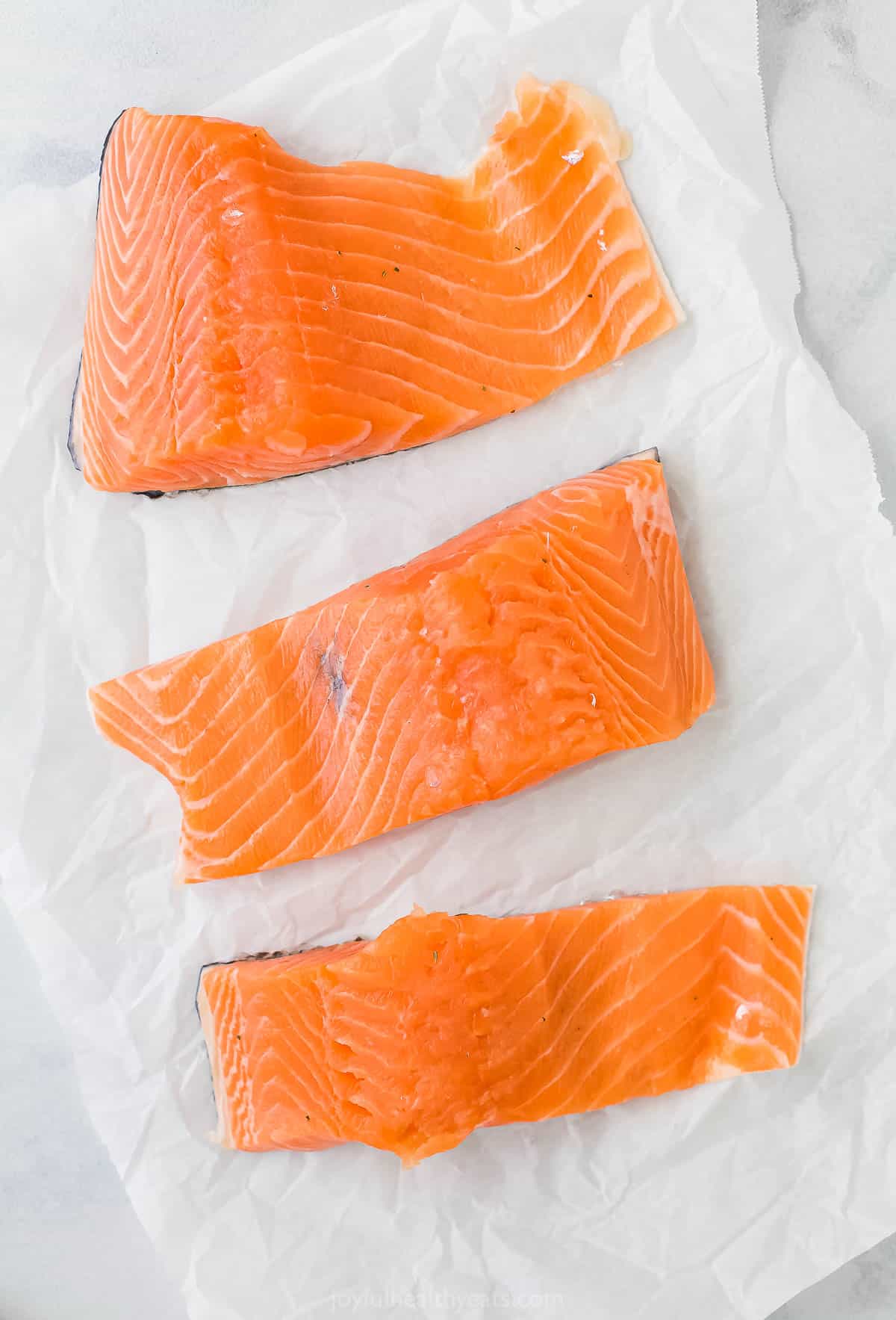 Three raw fish fillets on top of a piece of parchment paper.