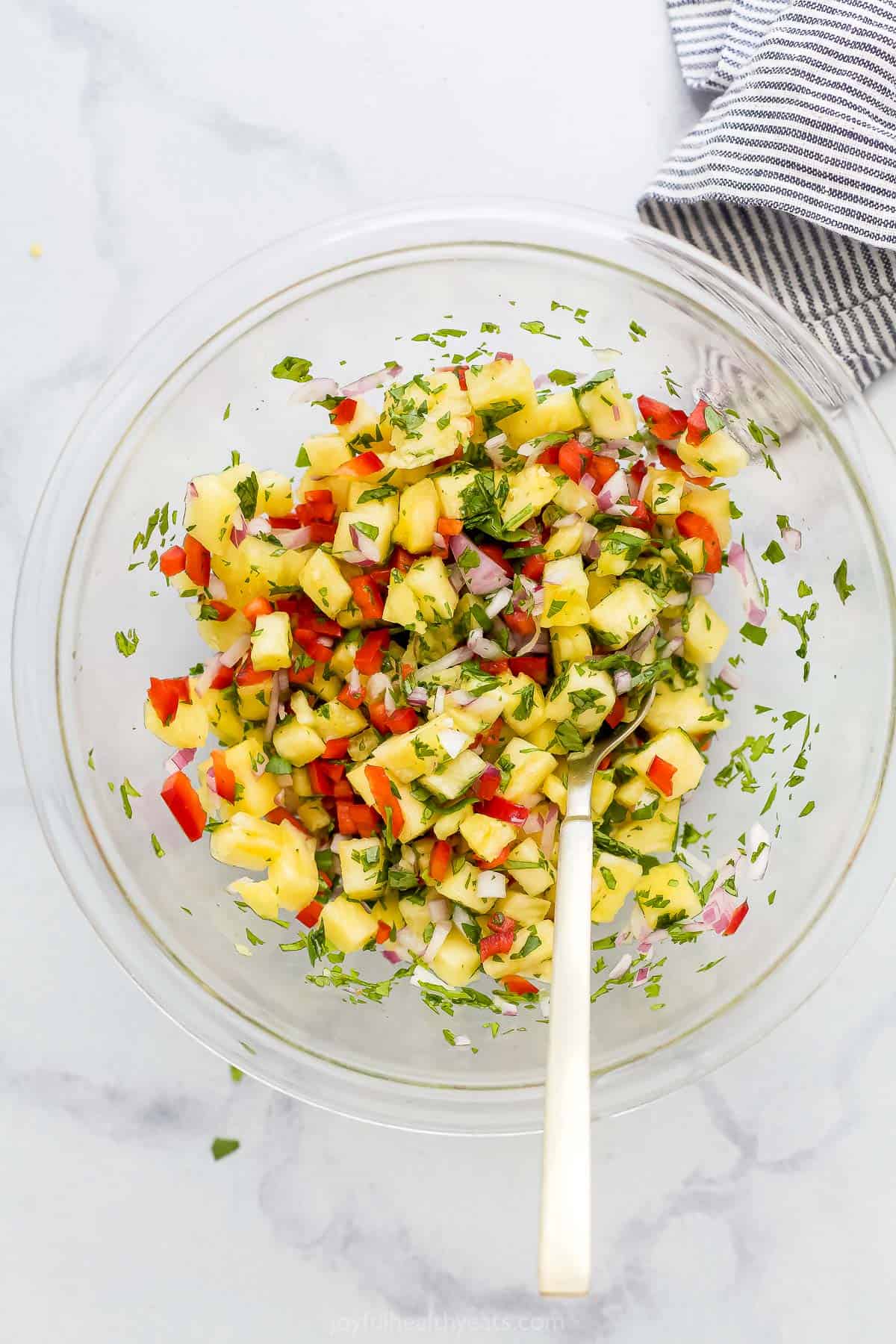 A clear glass mixing bowl full of homemade pineapple salsa.