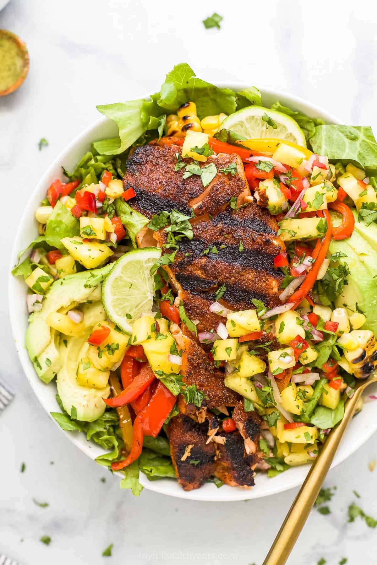 A blackened grilled fish salad in a bowl on top of a marble counter