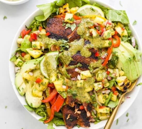 A bowl of salmon salad on a kitchen countertop beside a small dish of cilantro lime dressing