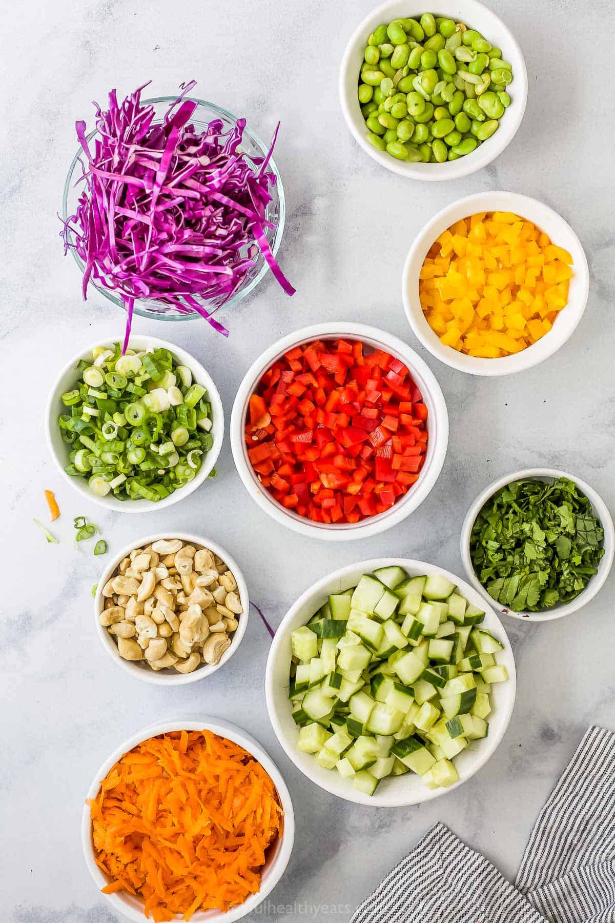 A bowl of shredded carrots, a bowl of chopped green onions and the rest of the prepared ingredients in separate bowls on a marble countertop