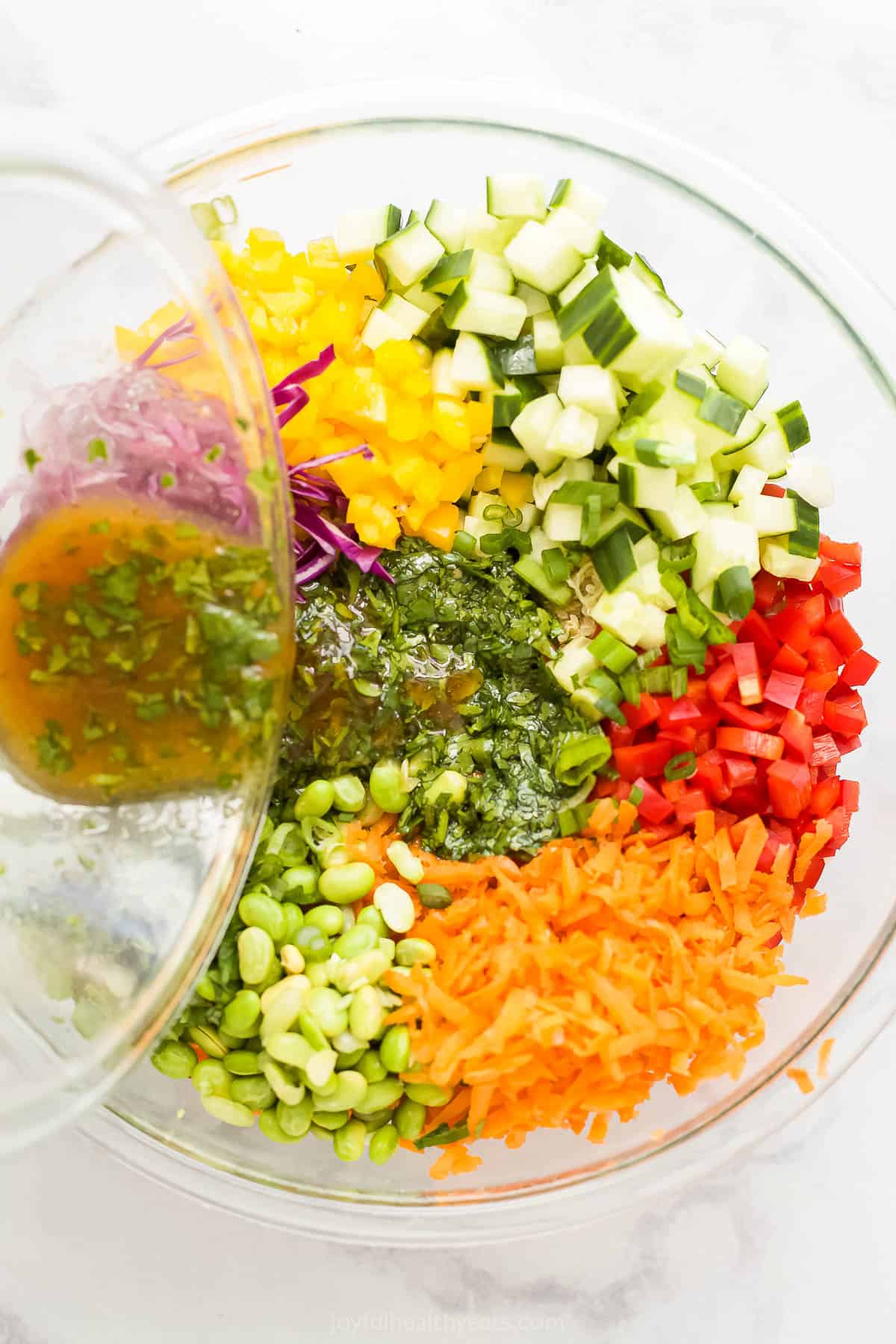 Sesame ginger dressing being poured over fresh veggies, nuts and herbs inside of a glass bowl