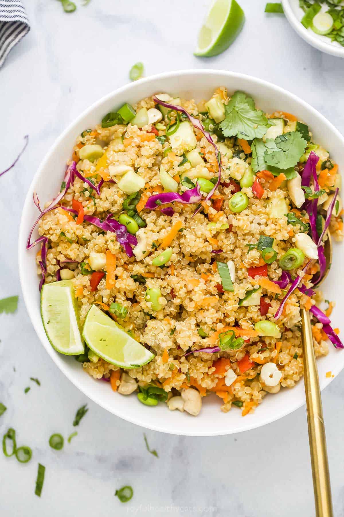 Thai quinoa salad in a bowl with two fresh lime wedges on top and a spoon digging into the salad