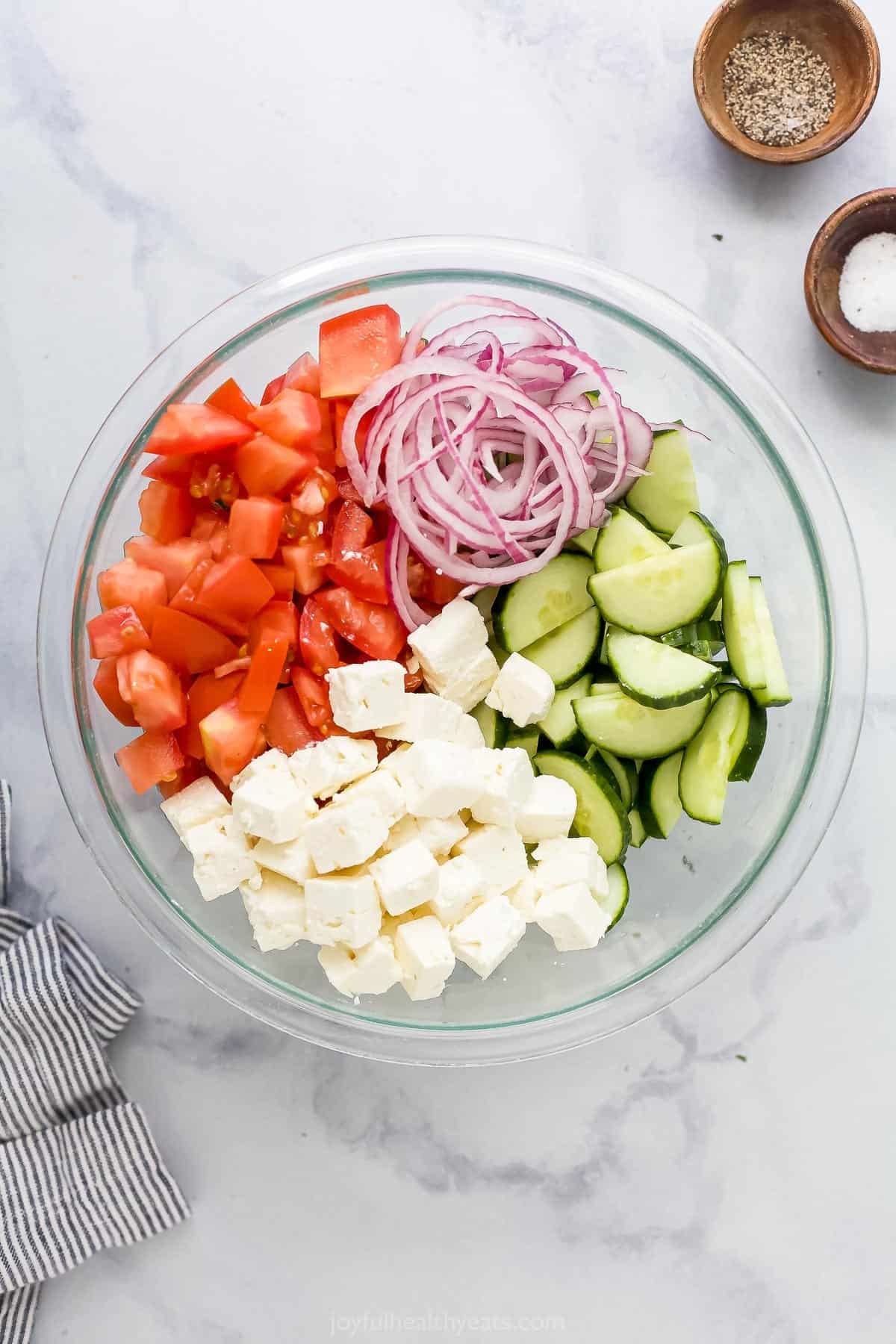 The prepared tomatoes, onions and cucumber in a bowl with the cubed feta cheese