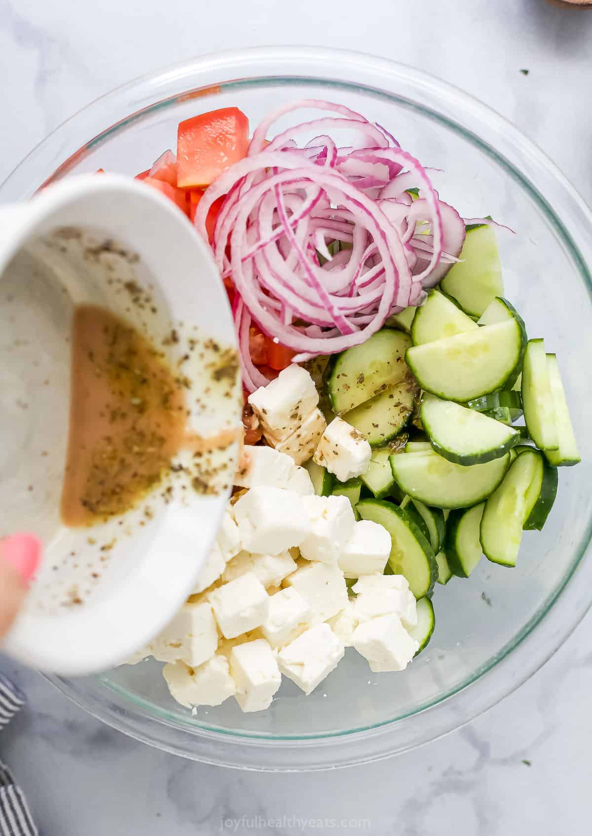 Red wine vinaigrette being poured into a mixing bowl full of veggies and feta cheese