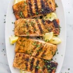 Four lemon pepper grilled salmon fillets lined up on a platter with fresh lemon wedges