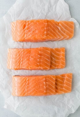 Three wild-caught salmon fillets lined up on a sheet of parchment paper.