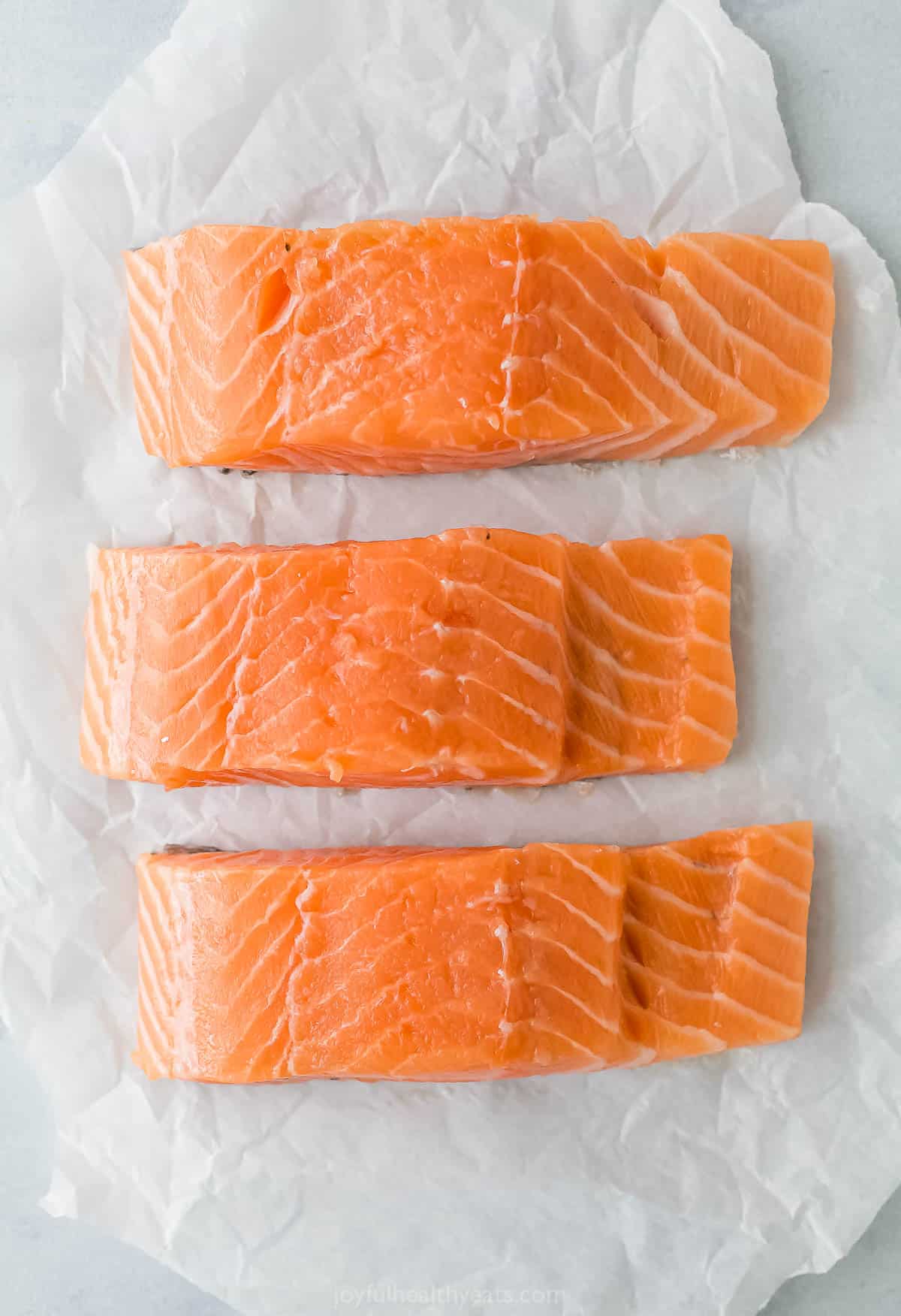 Three wild-caught salmon fillets lined up on a sheet of parchment paper