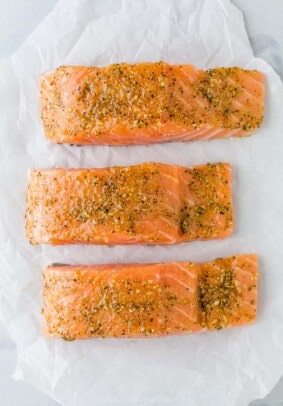 Three seasoned salmon fillets on a sheet of parchment paper.