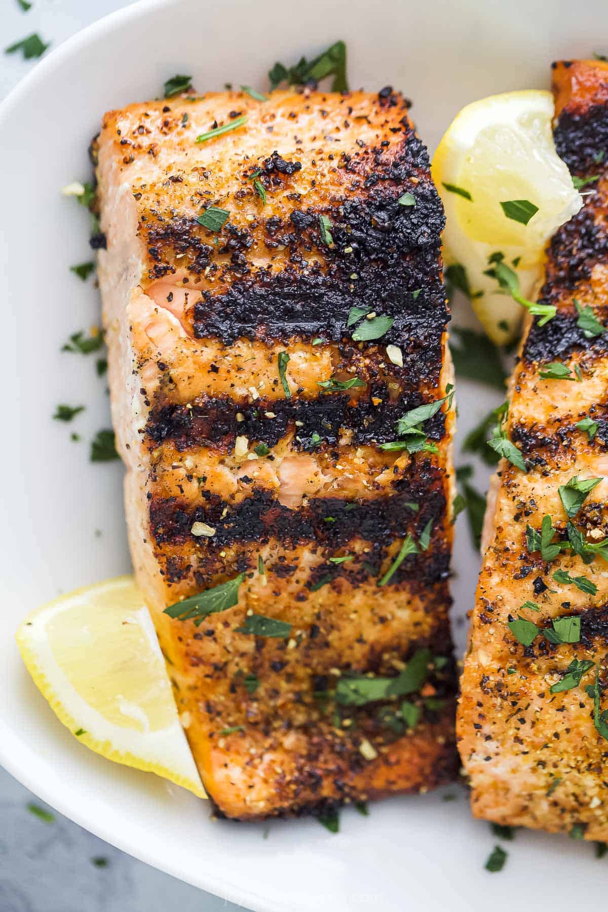 A lemon pepper salmon fillet on a plate with another fillet beside it.