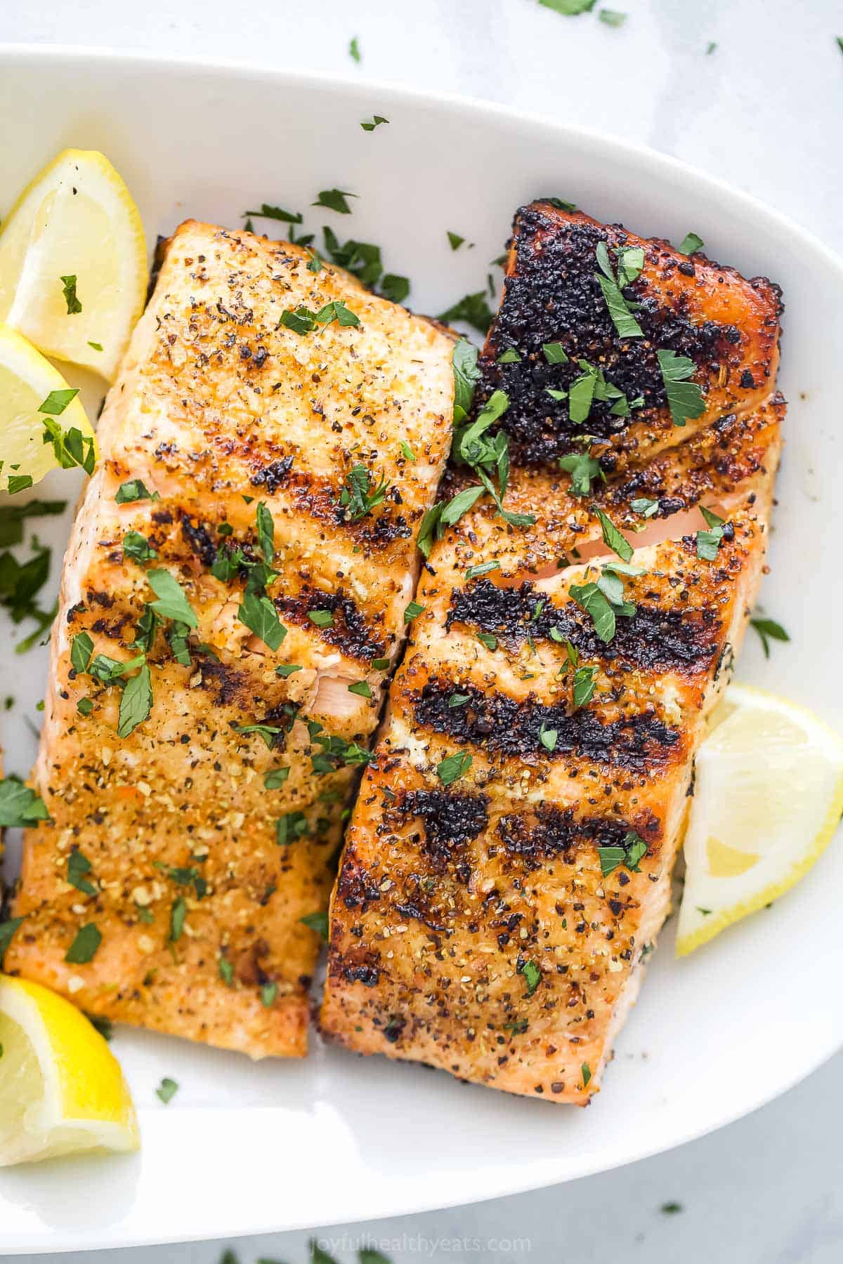 Two grilled citrus salmon fillets on a plate on top of a marble counter.