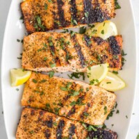 A long white serving platter holding four servings of grilled lemon pepper salmon