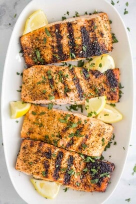 A long white serving platter holding four servings of grilled lemon pepper salmon