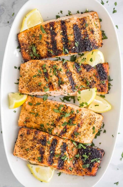 A long white serving platter holding four servings of grilled lemon pepper salmon