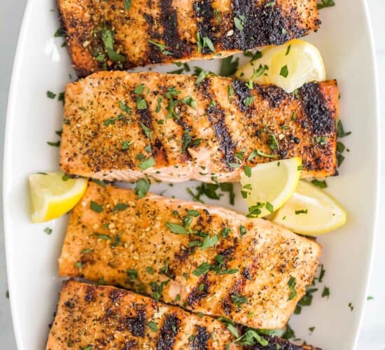 A long white serving platter holding four servings of grilled lemon pepper salmon
