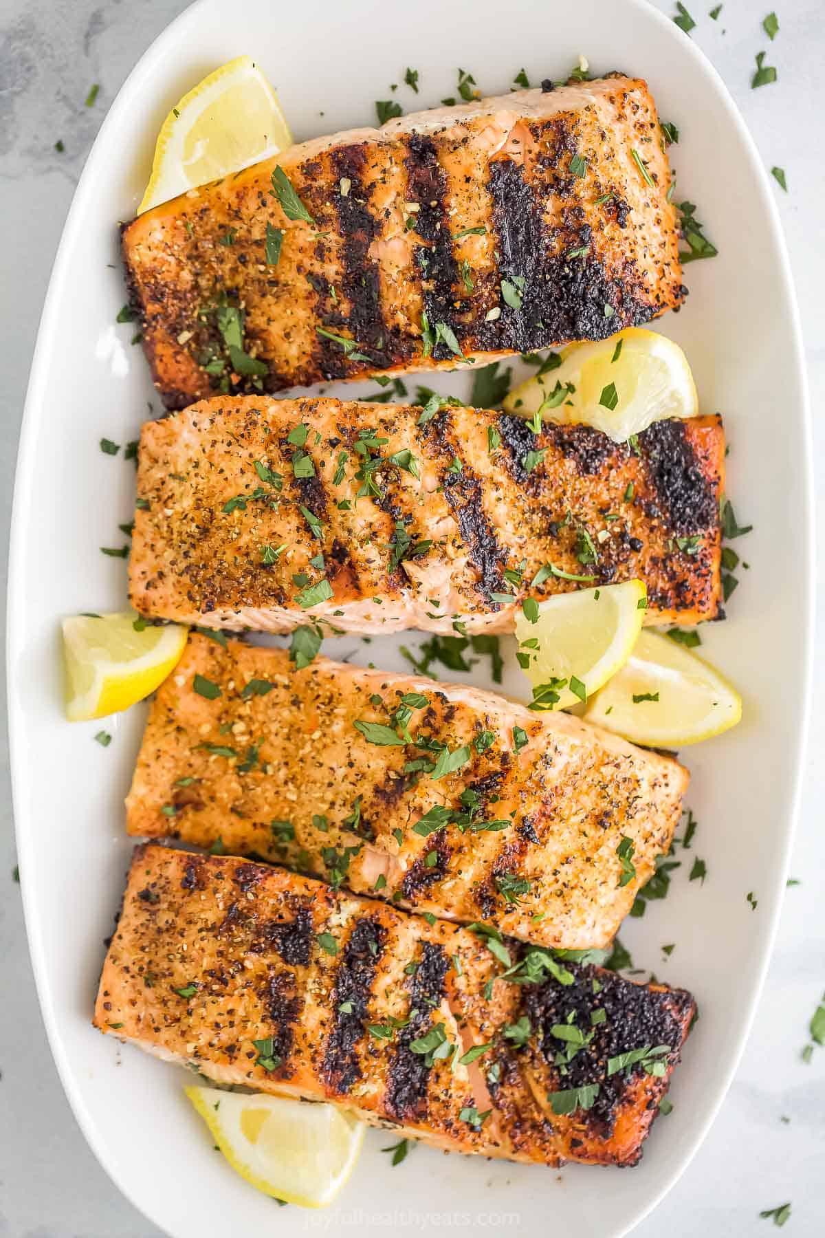 A long white serving platter holding four servings of grilled lemon pepper salmon.
