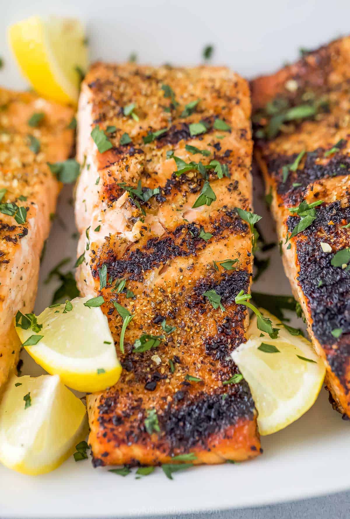 A close-up shot of three grilled fish fillets topped with fresh chopped parsley