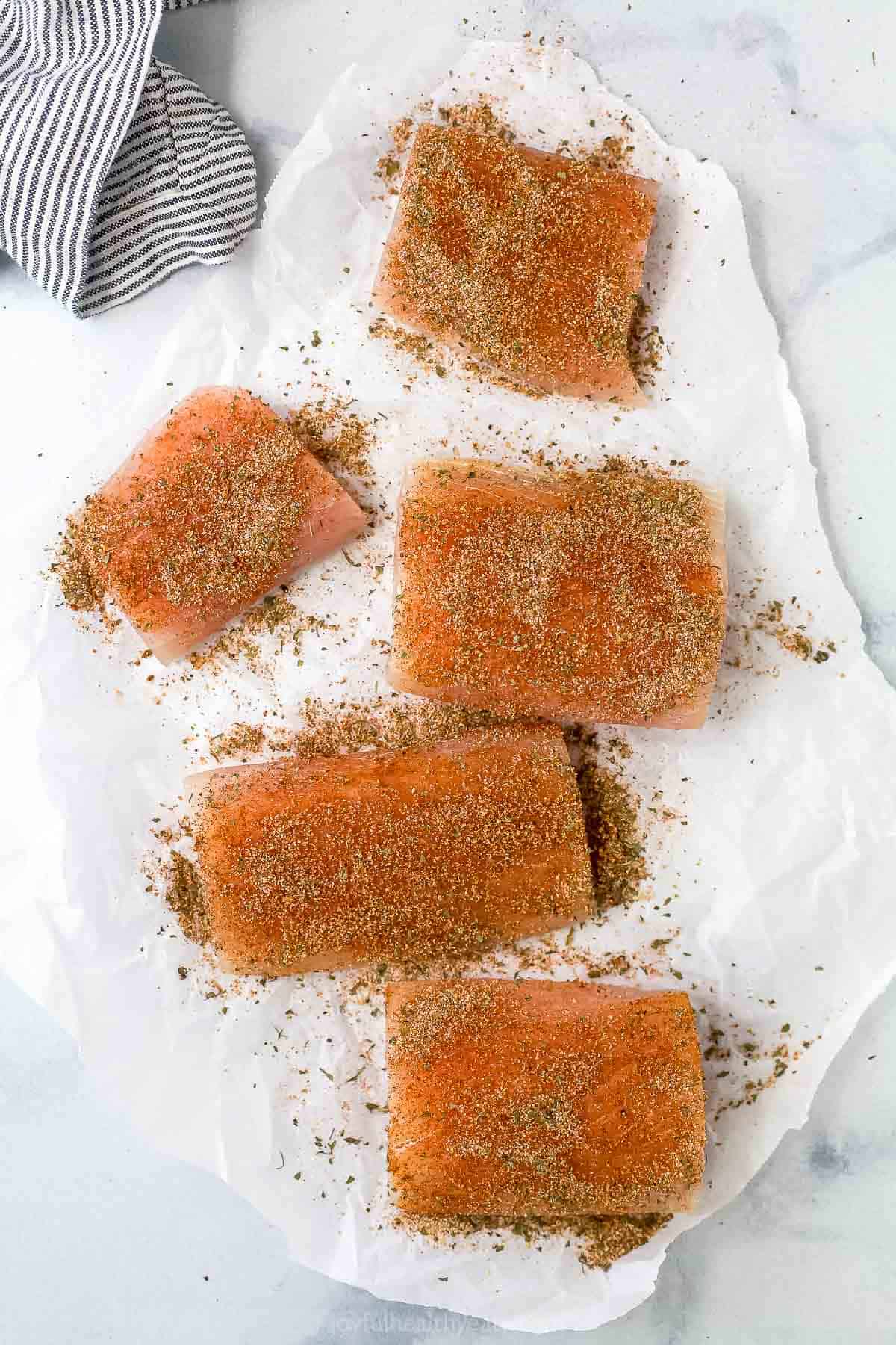 Seasoned mahi mahi sitting on a sheet of parchment paper beside a dishtowel