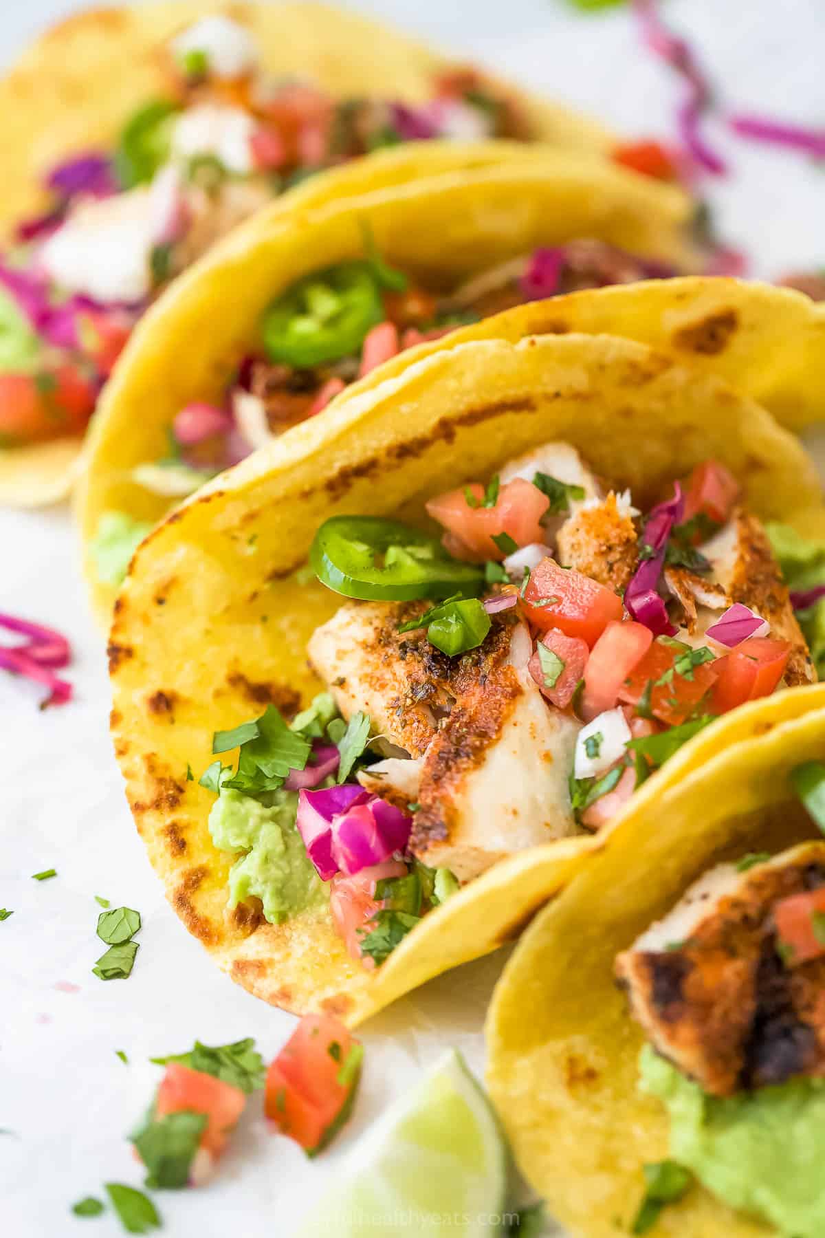 Four grilled mahi mahi tacos garnished with fresh chopped herbs and jalapeño slices