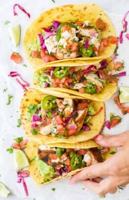 Four mahi mahi tacos lined up on a kitchen countertop with a hand grabbing one from the end of the line