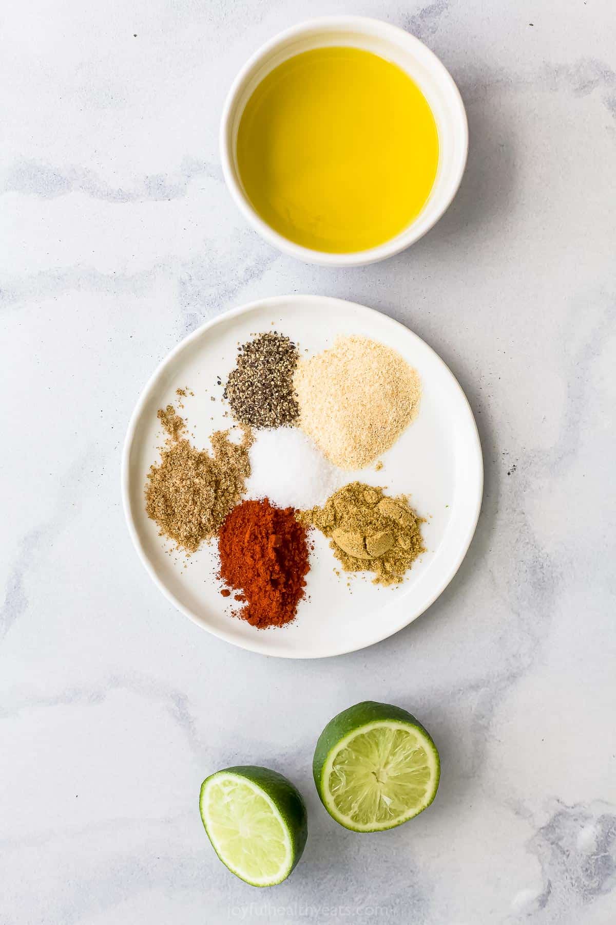 A fresh lime, a bowl of olive oil and all of the spice rub seasonings on a kitchen countertop
