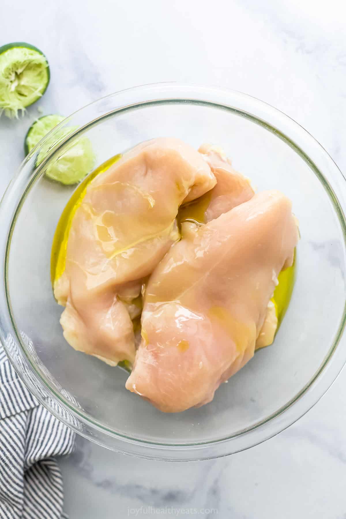 Raw chicken breasts inside of a mixing bowl with oil and lime juice