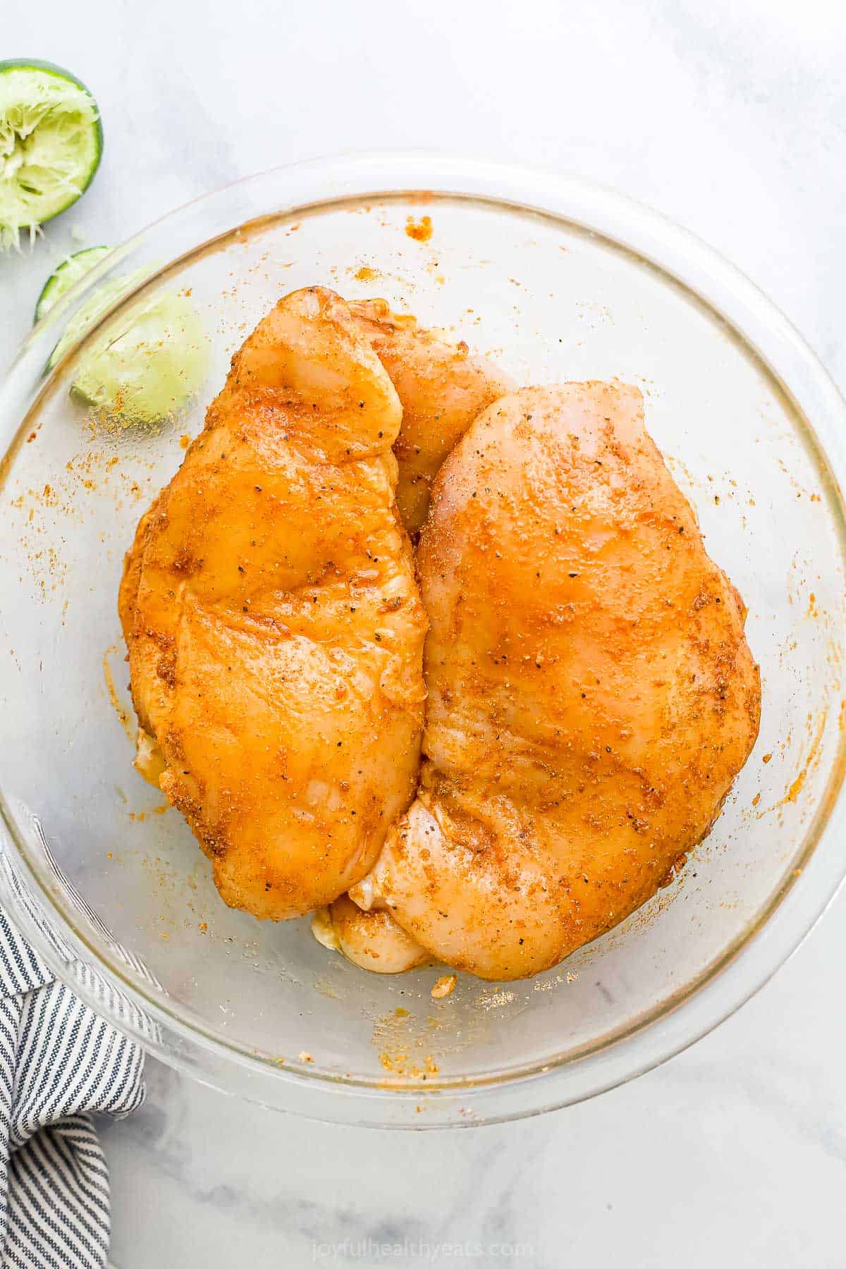 Seasoned chicken inside of a glass mixing bowl on a marble countertop