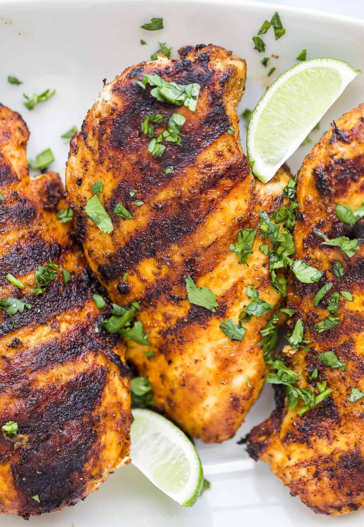 Grilled chicken on a plate with fresh lime wedges and chopped parsley